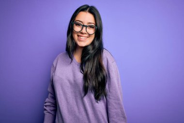 Mor izole edilmiş arka planda gözlük takan esmer, mutlu ve havalı bir gülümsemesi olan genç bir kadın. Şanslı kişi..