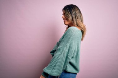 Moda kıyafetleri giyen genç ve güzel bir kadın. Manken, sokak tarzı giyiniyor. Pembe arka planda dikiliyor.