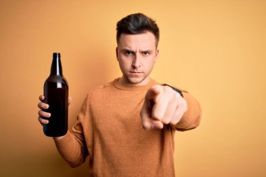 Sarı arka planda bira içen yakışıklı beyaz bir adam kamerayı işaret ediyor ve sen, el işareti, ön taraftan pozitif ve kendinden emin bir hareket.