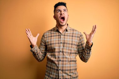 Genç yakışıklı adam izole sarı arka plan deli ve deli bağırarak ve agresif ifade ve kollar kaldırdı ile bağırıyor üzerinde duran rahat gömlek giyiyor. Hayal kırıklığı kavramı.