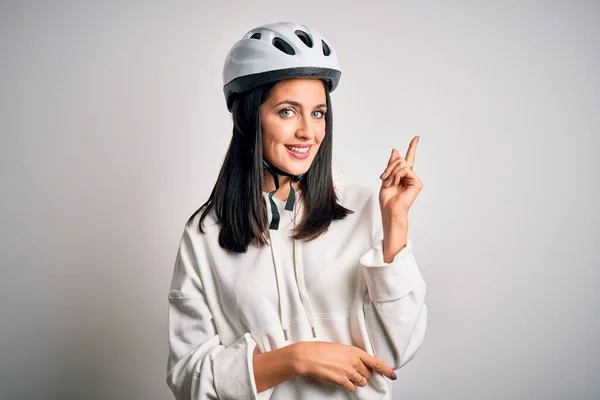 Young cyclist woman with blue eyes wearing bike helmet over isolated white background with a big smile on face, pointing with hand and finger to the side looking at the camera.