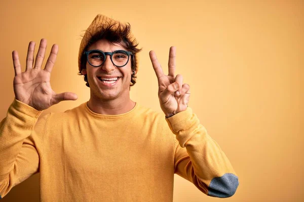 若いですハンサムな男身に着けていますカジュアルTシャツと眼鏡上の隔離された黄色の背景表示と指差す指番号7ながら笑顔自信と幸せ — ストック写真