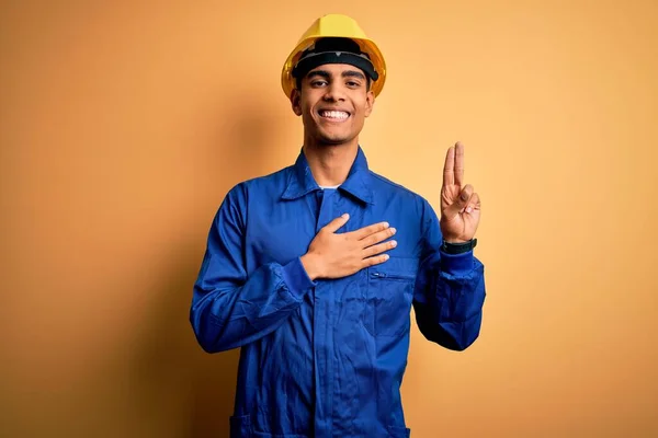 胸と指に手で身に着けている青の制服とセキュリティヘルメットを身に着けている若いハンサムなアフリカ系アメリカ人労働者の男 忠誠の誓いを作る — ストック写真