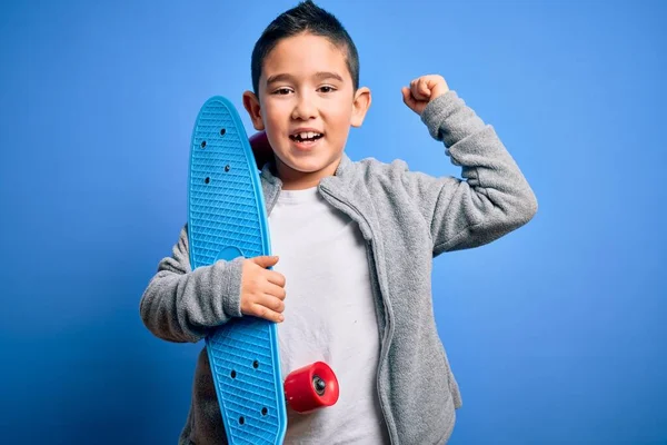 小男孩滑板手抱着现代滑板在蓝色孤立的背景上高喊着自豪 庆祝胜利和成功非常兴奋 欢呼着感情 — 图库照片
