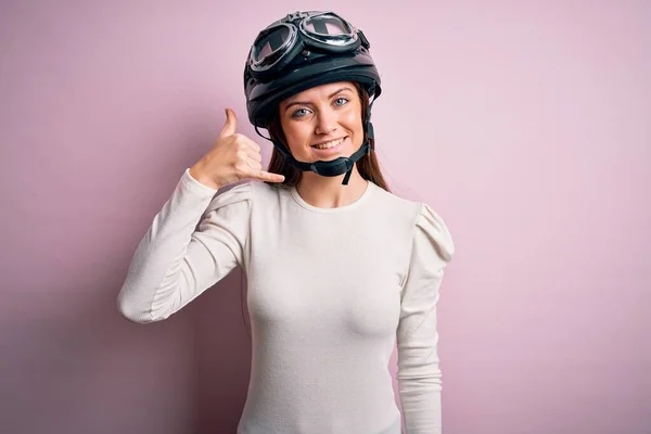 ピンクの背景に元ヘルメットをかぶって青い目をした若い美しいオートバイ愛好家の女性は 電話で話すような手や指で電話ジェスチャーをして笑っています 概念の伝達 — ストック写真