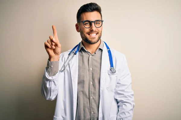 若いです医師男身に着けています眼鏡 医療白衣と聴診器上の隔離された背景を示し 指の番号1で指摘しながら 自信と幸せ — ストック写真