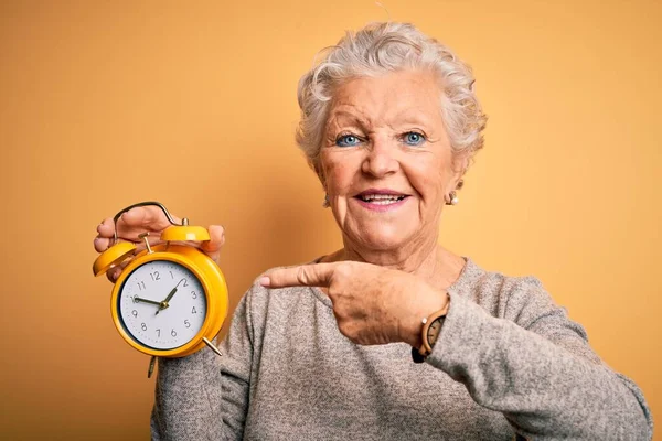 Sarı Arka Planda Çalar Saati Tutan Yaşlı Güzel Bir Kadın — Stok fotoğraf