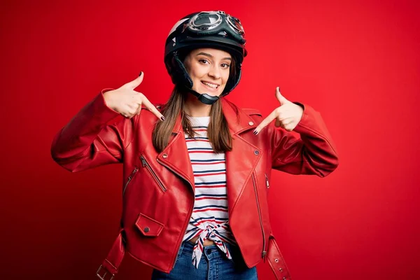 若い美しいブルネットのオートバイのヘルメットと顔に笑顔で自信を持って見える赤いジャケットを身に着けている自転車愛好家の女性は 指を誇りに思って幸せな自分自身を指して — ストック写真