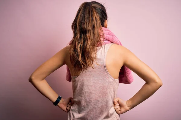 年轻美丽的黑发女运动员身穿运动服 披着粉色背景的毛巾 背对着身体 向后看去 — 图库照片