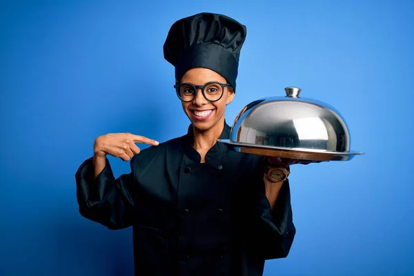 年轻的非洲女厨师 身穿制服 手持圆顶餐盘 手指指向自己 令人惊讶 — 图库照片