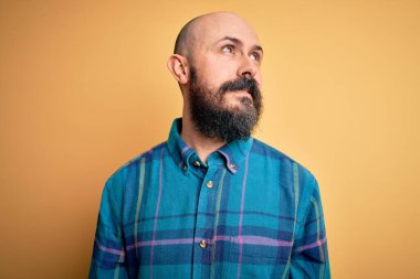 Sarışın, sakallı, sıradan tişörtlü, yalıtılmış sarı arka planda duran, yüzünde gülümseme, doğal bir ifade olan yakışıklı, kel bir adam. Kendinden emin gülen.