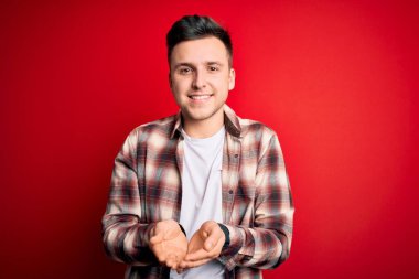 Kırmızı izole arka plan üzerine gündelik modern gömlekler giyen yakışıklı beyaz adam avuçlarını birbirine uzatarak gülümsüyor ya da el hareketi yapıyor. Tutun ve koruyun