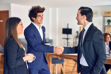 Mutlu ve kendinden emin gülümseyen genç ve güzel bir iş adamı grubu. Yüzünde gülümseme, kahve içmek ve ofiste el sıkışmak.