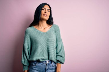 Moda kıyafetleri giyen genç ve güzel bir kadın. Manken, sokak tarzı giyiniyor. Pembe arka planda dikiliyor.