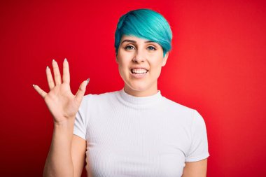 Mavi saçlı, kırmızı arka planda günlük tişörtler giyen genç ve güzel bir kadın beş numarayı gösterirken kendinden emin ve mutlu bir şekilde gülümsüyor..