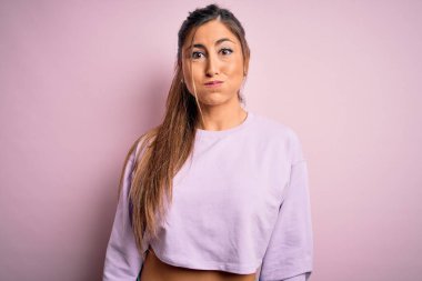 Pembe izole edilmiş arka plan üzerine kazak giyen genç ve güzel spor kadın komik yüzlü yanakları şişiriyor. Havayla şişmiş ağız, çılgın bir ifade..