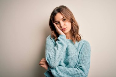Soyutlanmış arka planda günlük mavi süveter giyen genç sarışın kız kollarını kavuşturarak depresyondan sıkılmış ve yorgun görünüyor..