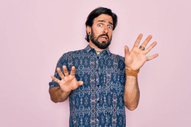 Pembe arka planda hippi tarzı giyinmiş genç, yakışıklı, bohem bir adam. Korku ifadesinden korkmuş ve dehşete düşmüş. El hareketlerini durdur, şok içinde bağır. Panik konsepti.