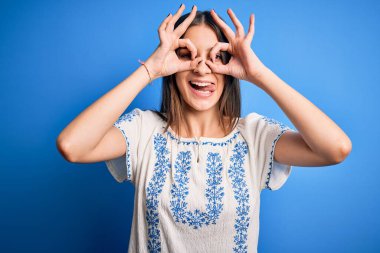 Genç, güzel, esmer, sıradan tişörtler giyen bir kadın mavi arka planda dikiliyor. Dürbün gibi güzel hareketler yapıyor. Gözleri parmaklarından bakıyor. Çılgın ifade.