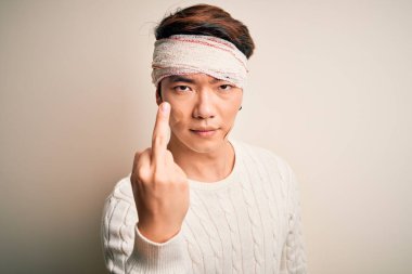 Young handsome chinese man injured for accident wearing bandage and strips on head Showing middle finger, impolite and rude fuck off expression