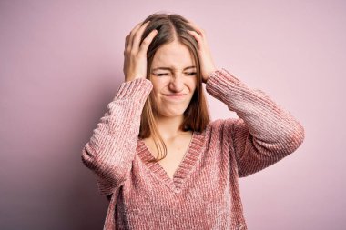 Genç, güzel, kızıl saçlı bir kadın izole edilmiş pembe arka plan üzerine günlük süveter giyiyor. Ağrı ve migren yüzünden baş ağrısı ve stresten muzdarip. Ellerini başının üstüne koy..