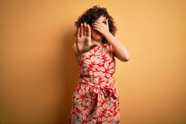 Genç ve güzel kıvırcık Arap kadın tatilde. Çiçekli bir elbise giyiyor ve güneş gözlüğü takıyor. Gözlerini ellerle kapatıyor. Utanç verici ve olumsuz bir kavram..