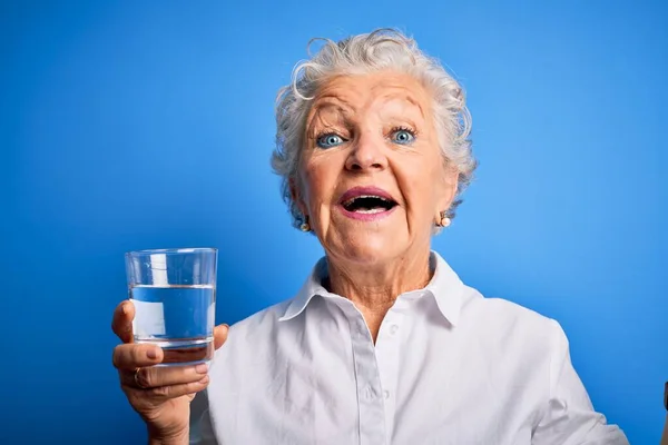 Senior Vacker Kvinna Dricka Glas Vatten Stående Över Isolerad Blå — Stockfoto