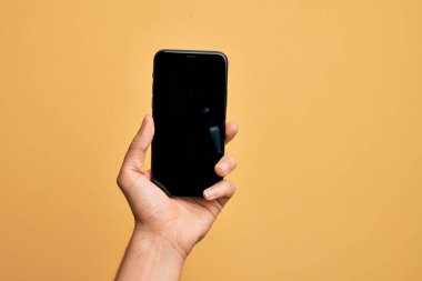 Kafkasyalı genç adam elinde akıllı telefonuyla izole edilmiş sarı arka planda ekranı gösteriyor.