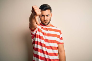 İzole edilmiş beyaz arka plan üzerinde duran sıradan çizgili tişört giyen genç ve yakışıklı bir adam mutsuz, reddedilmiş ve olumsuz jest yapmış görünüyor. Kötü ifade.