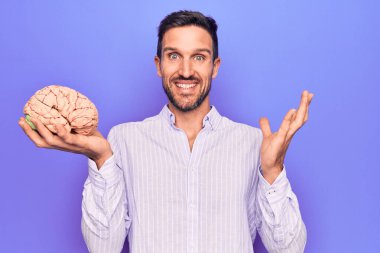 Genç yakışıklı adam hafızasını korumak istiyor beyni soyutlanmış mor arka planda tutarak başarıyı mutlu bir gülümsemeyle ve kazanan yüz ifadesiyle el kaldırarak kutluyor.