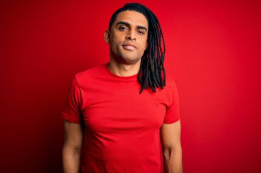 Kırmızı günlük tişört giyen Afro-Amerikan Afrikalı genç yakışıklı adam yüzünde ciddi bir ifadeyle rahatlamış. Basit ve doğal bir şekilde kameraya bakıyorsun..