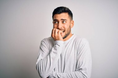 İzole edilmiş beyaz arka plan üzerinde sıradan tişörtler giyen genç yakışıklı adam elleri ağız yiyen tırnaklarla stresli ve gergin görünüyor. Endişe sorunu.