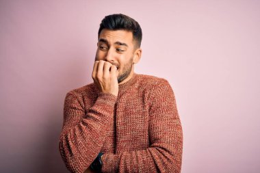 İzole edilmiş pembe arka plan üzerinde duran sıradan süveter giyen genç yakışıklı elleri ağız yiyen tırnaklarla stresli ve gergin görünüyor. Endişe sorunu.