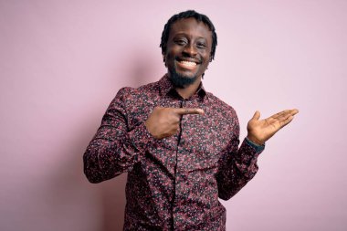 Genç, yakışıklı, Afro-Amerikalı bir adam pembe arka plan üzerinde dikilmiş kameraya hayret ediyor ve gülümsüyor..