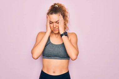 Mavi gözlü genç, güzel sarışın spor kadın spor giyiniyor. Spor kıyafetleri giyiyor. Ağrı ve migren yüzünden çaresiz ve stresli. Ellerini başının üstüne koy..