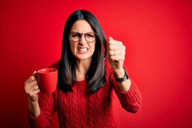 Mavi gözlü, gözlüklü ve kahve içen genç esmer kadın öfkeyle bağırıyor, deliriyor ve el kaldırarak bağırıyor, öfke konsepti oluşturuyor.