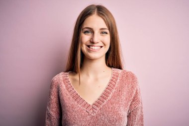 Genç, güzel, kızıl saçlı bir kadın izole edilmiş pembe arka plan üzerine günlük süveter giyiyordu. Yüzünde mutlu ve havalı bir gülümseme vardı. Şanslı kişi..