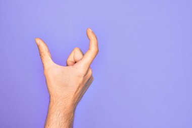 İzole edilmiş mor arka plan üzerinde parmaklarını gösteren beyaz bir adamın eli. Görünmez bir şeyi alıyor, parmakları boşluğu gösteren bir nesneyi tutuyor.