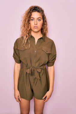 Mavi gözlü genç bir kadın pembe arka planda günlük yazlık elbiseler giyiyor ve yüzünde ciddi bir ifade var. Basit ve doğal bir şekilde kameraya bakıyorsun..