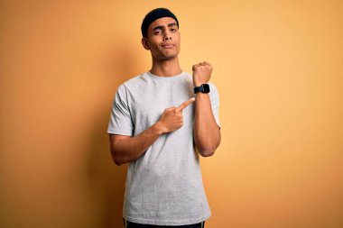 Sarı arka plan üzerine spor giyerek spor yapan yakışıklı Afro-Amerikan sporcusu. Saati, sabırsızlığı izlemek için acele ediyor ve rahat bir ifadeyle kameraya bakıyor.