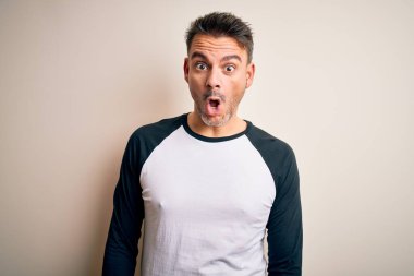 İzole edilmiş beyaz arka plan üzerinde duran sıradan tişört giyen genç yakışıklı adam korku, şaşkınlık ifadesi ve heyecanlı yüz ifadesiyle dehşete düşmüş ve şok olmuştu..