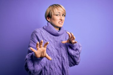 Kış balıkçı yaka kazak giyen kısa saçlı genç sarışın kadın. Mor arka planda iğrenç bir yüz ifadesi var. Tiksinti reaksiyonu yüzünden tiksinti ve korku dolu bir ifade takınıyor..