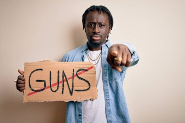 Young african american man asking for peace holding banner with prohibited guns message pointing with finger to the camera and to you, hand sign, positive and confident gesture from the front clipart