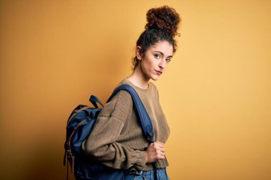 Kıvırcık saçlı ve piercingli genç ve güzel bir kız öğrenci. Sırt çantası takıyor. Yüzünde kendine güvenen bir ifade var.