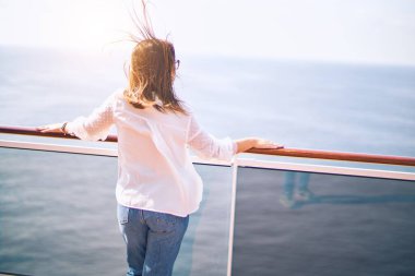 Genç ve güzel bir kadın bir gemi güvertesinde durmuş sırıtarak gemi seyahati yapıyor.