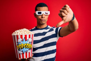 Genç ve yakışıklı Afro-Amerikalı adam film izlerken 3D gözlük takıyor patlamış mısır yiyor mutsuz görünüyor, reddedilmiş ve olumsuz bakıyor. Kötü ifade.