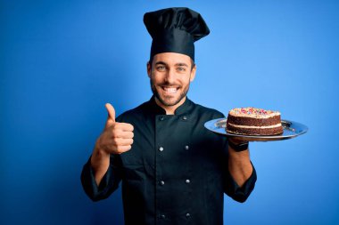 Sakallı, üniformalı, şapkalı, elinde pasta tepsisi olan, gülümseyen genç yakışıklı tencereci.