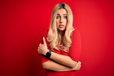 Genç, güzel, sarışın bir kadın. Günlük tişört giyiyor. İzole edilmiş kırmızı arka planda duruyor.