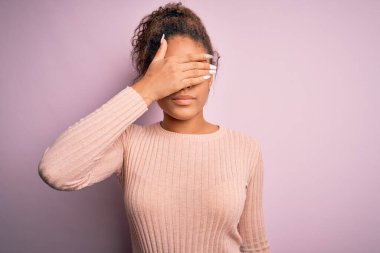 Genç, güzel, Afro-Amerikalı bir kız pembe arka planda dikilmiş ciddi ve üzgün gözlerle gözlerini kapatıyor. Görme, saklama ve reddetme konsepti
