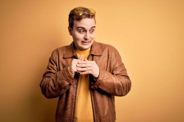 Sarı arka planda rahat deri ceket giyen genç ve yakışıklı bir adam gergin ve heyecanlı bir şekilde çenesinin kenarına bakıyor.